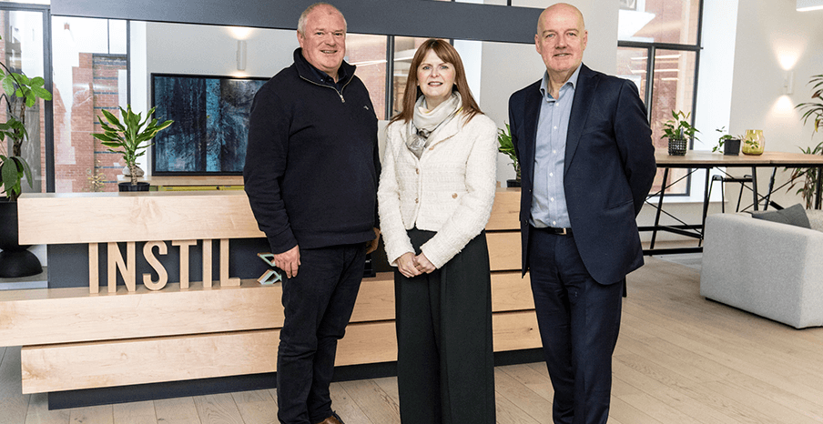 Two men and a woman are standing in an office space, posing for a photo together 