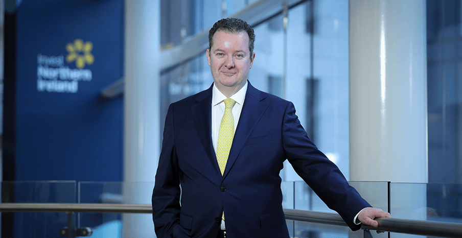 Kieran Donoghue, Invest NI CEO, is standing on a balcony in front of the Invest NI logo