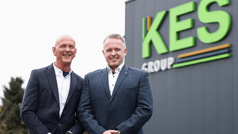 Two men standing in front of KES Group sign on factory 
